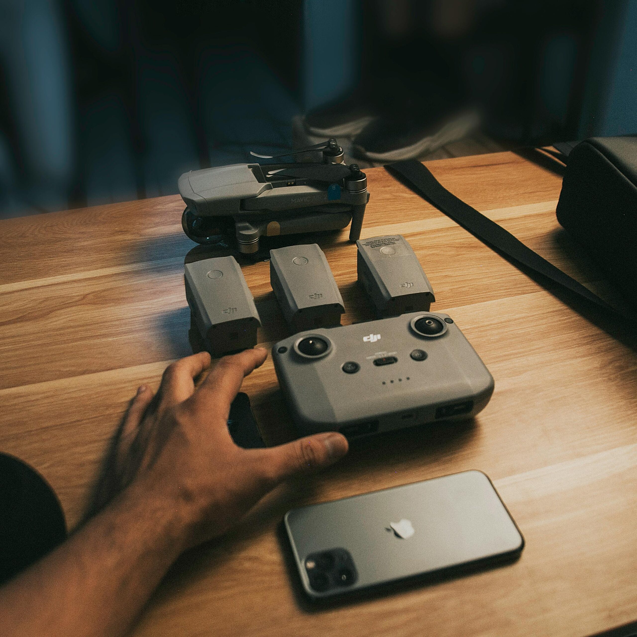 Close-up of a drone with batteries, controller, and smartphone on wooden table, ready for setup.